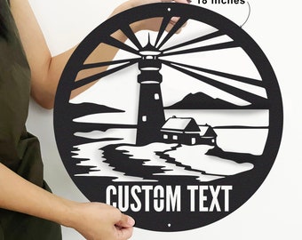 Könnte beinhalten: Schwarze Metall-Wandkunst mit Leuchtturm-Motiv, 45,7 cm Durchmesser, mit Küstenlandschaft. Der Text "CUSTOM TEXT" ist unten zu sehen. Die Wandkunst wird von einer Person gehalten.