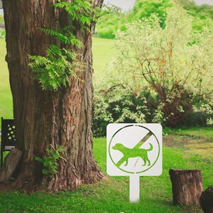 May include: White metal sign with a green silhouette of a dog and a diagonal line through it. The sign reads "No Dogs" and is mounted on a white metal post.