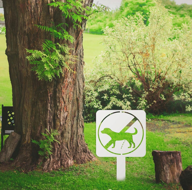 May include: White metal sign with a green silhouette of a dog and a diagonal line through it. The sign reads "No Dogs" and is mounted on a white metal post.