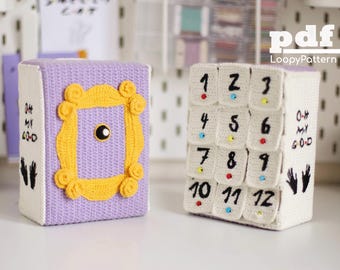 May include: Two crocheted boxes, one purple with a yellow frame and the other white with black numbers 1-12. Both boxes have the text "Oh My God" and a handprint.
