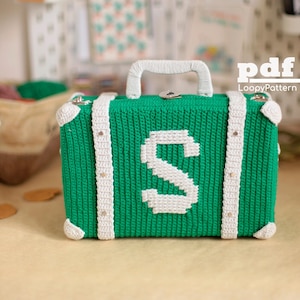 May include: A rectangular crochet suitcase in vibrant green with white accents, featuring a prominent white letter S on the front, a white top handle, and white corner reinforcements. The text pdf LoopyPattern is visible in the upper right corner.