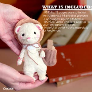 Op de afbeelding: Een gehaakte amigurumi witte muis met een roze en bruine hoed en een roze gehaakte tas. De muis wordt vastgehouden door de handen van een persoon. De afbeelding bevat de tekst "WHAT IS INCLUDED:" en een lijst met items die zijn inbegrepen in het haakpatroon.