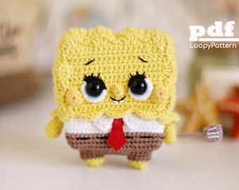 May include: A handmade crochet figure of a cartoon character with a yellow sponge-like body, brown pants, a white shirt, and a red tie. The figure has large black eyes, eyelashes, and a small smile. The text "pdf LoopyPattern" is visible.