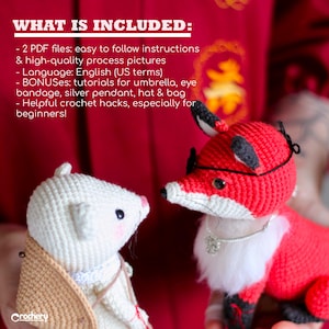 May include: Two crocheted amigurumi toys, a white mouse and a red fox, are facing each other. The mouse is wearing a brown hat and a silver necklace. The fox is wearing a black eye patch and a silver necklace with a charm. The background is a red fabric with Chinese characters.