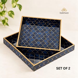 May include: A set of two square trays featuring a deep blue surface with a gold-coloured quatrefoil pattern and gold-coloured edges. The text IndiAure and SET OF 2 are visible. The trays have a glossy finish and a structured, raised border design.