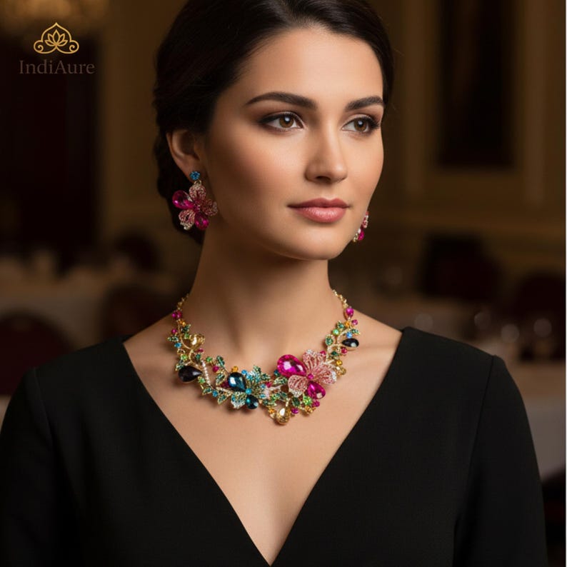 May include: A colorful floral necklace and matching earrings. The jewelry features pink, blue, green, and yellow gemstones set in a gold-tone metal. The necklace and earrings are worn by a person wearing a black dress.