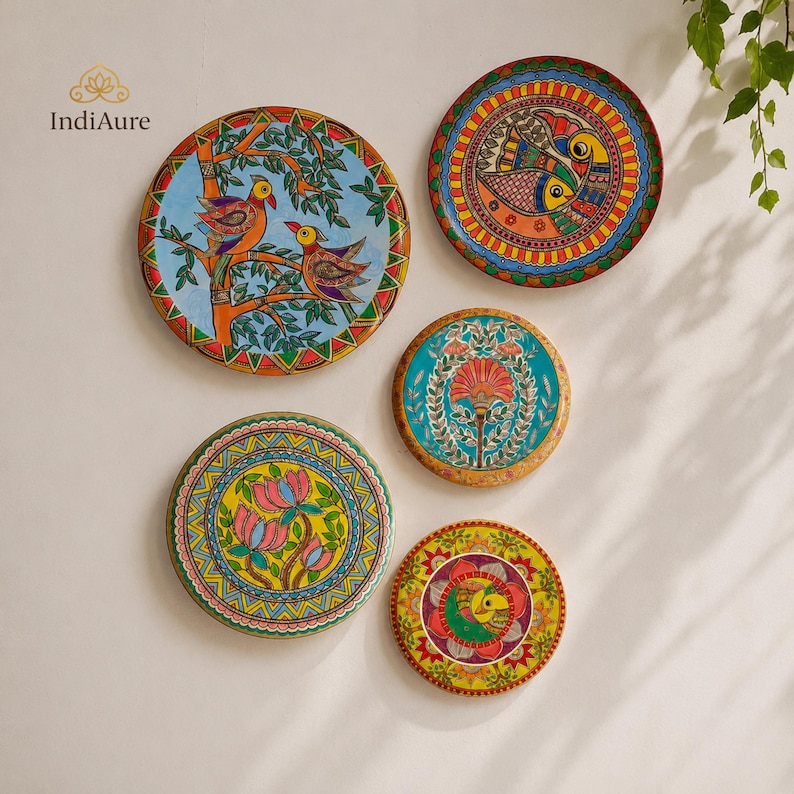 May include: Five circular decorative plates featuring vibrant hand-painted designs. The artwork includes birds on branches, stylized fish, a central floral motif, pink lotus flowers, and a geometric mandala pattern in bright colors.