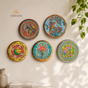 May include: Five circular wall plates featuring vibrant hand-painted designs. The plates display colorful motifs including stylized birds, floral patterns, and intricate geometric borders in shades of orange, blue, green, yellow, and pink.