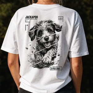 May include: A white t-shirt featuring a black and white graphic of a Jackapoo dog on the back. The design includes the text JACKAPOO, CLEVER. PLAYFUL. LOYAL., and CANINE HYBRID X-POO UNIT, along with diagonal lines and geographic coordinates.