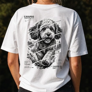 Puede incluir: Una camiseta blanca con un gráfico en blanco y negro en la parte posterior de un perro Cavapoo. El diseño incluye líneas diagonales, un fondo de bosque y el texto Cavapoo, Charm in Every Step, Origin: Love, Scale: 100% y Cavapoo Unit.