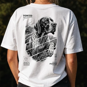 Könnte beinhalten: Ein weißes T-Shirt mit einer schwarz-weißen Grafik eines Pointers auf der Rückseite. Das Design enthält den Text "POINTED BUILT TO LOCATE", "FIELD OPS POINTER", "39.1237 N 94.5786 W" und "SPEC 07" mit einem Fadenkreuz und diagonalen Linien.