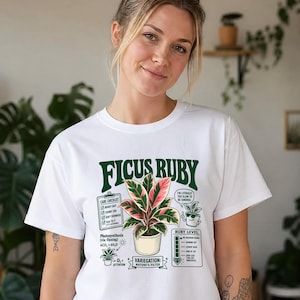 Könnte beinhalten: Ein weißes T-Shirt mit einer Grafik einer Ficus Ruby Pflanze im Topf. Das Design enthält den Schriftzug Ficus Ruby, eine Pflege-Checkliste, eine Rubinstufen-Anzeige sowie wissenschaftliche Notizen zur Photosynthese in Grün und Pink.