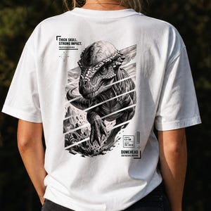 Może przedstawiać: Biały t-shirt z czarno-białą grafiką dinozaura Pachycephalosaurus na plecach. Nadruk zawiera tekst "THICK SKULL. STRONG IMPACT.", "PACHYCEPHALOSAURUS", "DOMEHEAD", "CRETACEOUS DIVISION" oraz "LENGTH 4.5-5M, WEIGHT 450-500 KG".