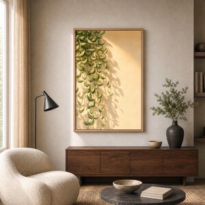 Puede incluir: Una pieza de arte mural rectangular enmarcada que presenta una ilustración vertical de una planta verde colgante con hojas variegadas sobre un fondo amarillo claro sólido, proyectando sombras distintas que imitan la forma de la planta.