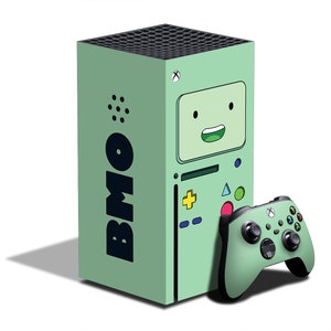 May include: A mint green Xbox Series X console and matching controller. The console features a cartoon character design with the text "BMO" in black. The controller has a variety of colored buttons and directional pad.