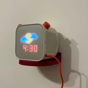 May include: A white and orange digital clock with a red LED display showing the time 4:30. The clock is mounted on a red shelf and has a red cord.