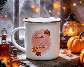 May include: A white enamel mug with a silver rim featuring a watercolor-style pink circle, a small brown mushroom, orange and red maple leaves, and the text Hello Autumn in black script, set against a window with pumpkins and glass bottles.