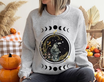 May include: A gray sweatshirt with a black raven and moon phases graphic. The graphic features a raven perched on a branch with flowers and leaves. The moon phases are depicted in a circle around the raven.