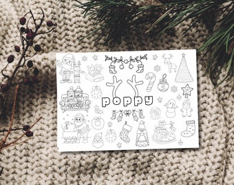 May include: A white card featuring black line drawings of Christmas illustrations, such as Santa Claus, reindeer, baubles, and a Christmas tree. The name "poppy" is in the centre. The card rests on a knitted surface.