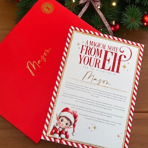 Puede incluir: Un sobre rojo con el nombre "Mason" en letras doradas, junto a una carta con una ilustración de elfo festivo. La carta dice "A Magical Note From Your Elf" y está decorada con detalles dorados y rojos.