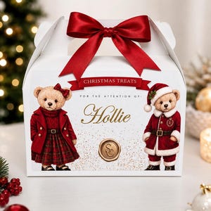 Könnte beinhalten: Eine weiße Schachtel mit einer roten Satinschleife oben. Auf der Vorderseite sind zwei Teddybären abgebildet, einer in rotem Mantel und kariertem Rock, der andere im Weihnachtsmannkostüm. Der Text lautet CHRISTMAS TREATS, FOR THE ATTENTION OF: Hollie.