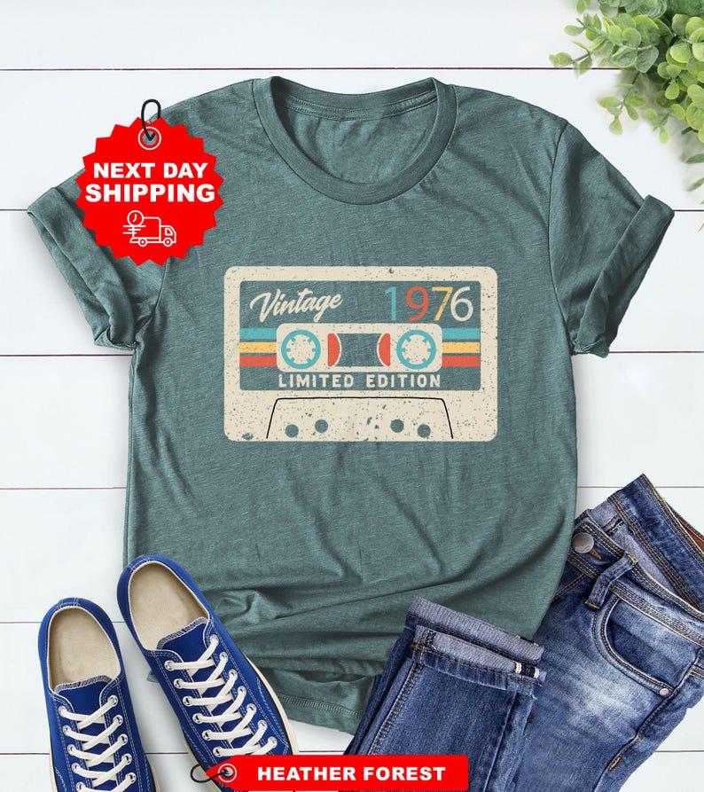 Op de afbeelding: Heather forest green t-shirt met een vintage cassettebandje ontwerp met de tekst "Vintage 1976 Limited Edition". De afbeelding toont ook een blauwe jeans en blauwe sneakers.