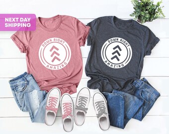 May include: Two t-shirts with the text "Down Right Amazing" and an arrow graphic. The shirts are in pink and dark gray.