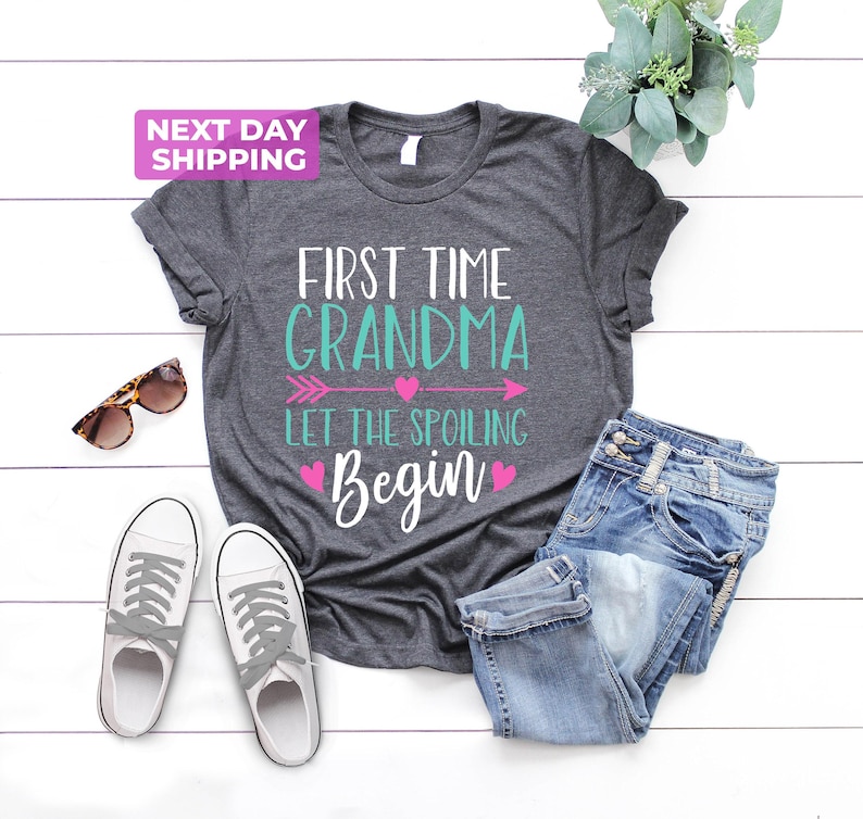 May include: Gray t-shirt with the text "First Time Grandma Let The Spoiling Begin" in turquoise and pink with a pink arrow and hearts.