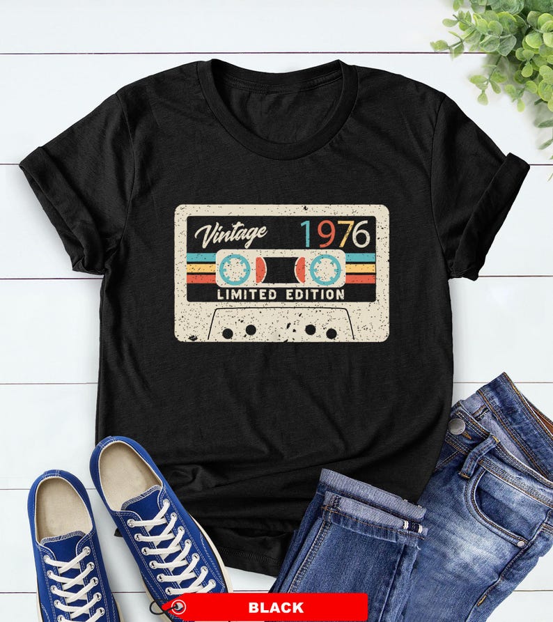 Op de afbeelding: Zwart T-shirt met een vintage cassettebandje ontwerp. Het ontwerp bevat de tekst "Vintage 1976 Limited Edition" in retro kleuren. Het shirt wordt gecombineerd met een blauwe jeans en blauwe sneakers.
