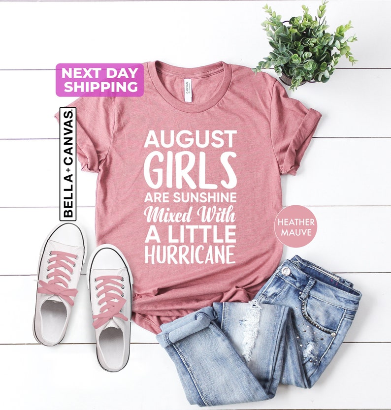 August birthday shirt featuring the phrase "August Girls Are Sunshine Mixed With a Little Hurricane" in bold white typography. Birthday graphic tee for August-born women, sisters, daughters, moms, and friends celebrating their birth month.