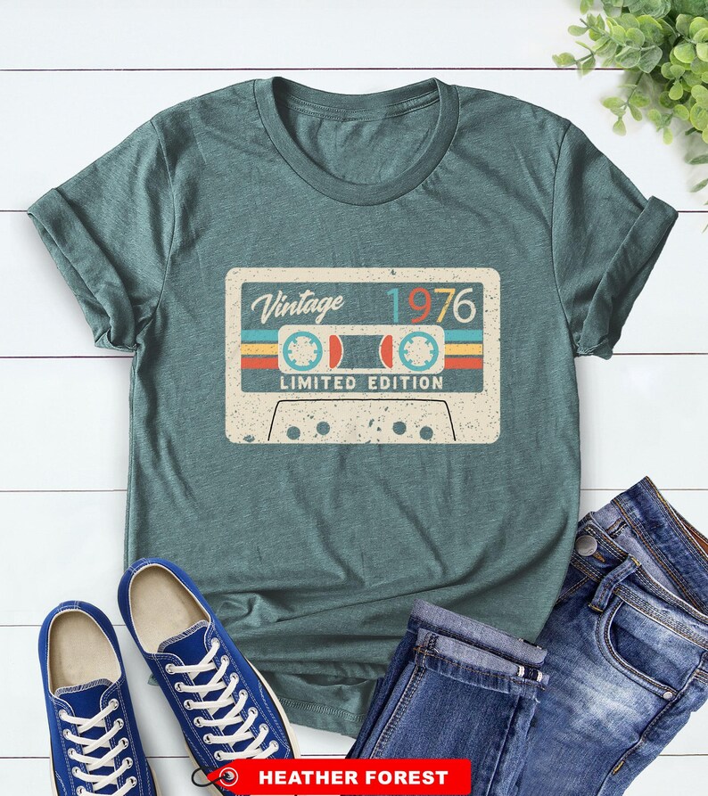 Op de afbeelding: Een tealkleurig T-shirt met een vintage cassettebandje ontwerp met de tekst "Vintage 1976 Limited Edition". Het shirt wordt gecombineerd met een blauwe jeans en blauwe sneakers. Het shirt is gemaakt van Heather Forest materiaal.
