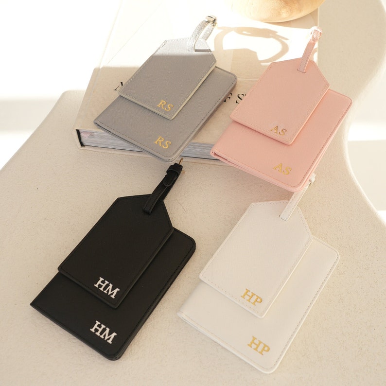 May include: Four leather luggage tags with gold lettering. The tags are in grey, pink, black, and white. The letters on the tags are "RS", "AS", "HM", and "HP".
