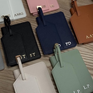 May include: A selection of personalised luggage tags and passport holders in colours such as black, pink, navy, and green. Each tag and holder has gold-coloured hardware and initials.