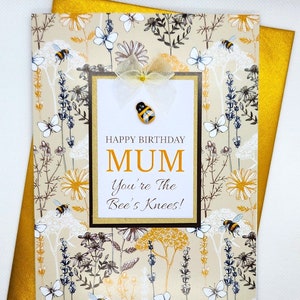 May include: A beige card with a floral pattern featuring bees and butterflies. The card has a white rectangle with the text "Happy Birthday Mum You're the Bee's Knees!" and a small bee embellishment.