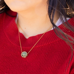 May include: A gold chain necklace with a round pendant featuring a green stone.