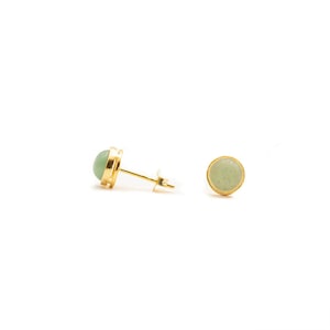 May include: A pair of gold stud earrings with a light green stone in each. The earrings are simple and elegant.