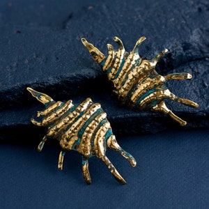 Bold earrings in the form of lond ribbed shell with spikes on the side. Earrings are hand-made from the brass sheet using hammers and other tools. Earrings are a bit mismatched due to their artisan nature. They have a silver ear wire.