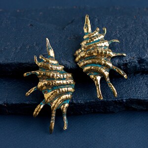 Big earrings in the form of oval ribbed shell with spikes on one side. Earrings are completely hand-made from the brass sheet using hammers and other tools. Earrings are simmetrical and a bit mismatched due to their artisan nature.