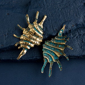 Big long earrings in the form of elongated ribbed shell with spikes on one side. Earrings are simmetrical and a bit mismatched due to their artisan nature. Photo shows them from front and back side, it is seen that brass has blue patina in hollows.