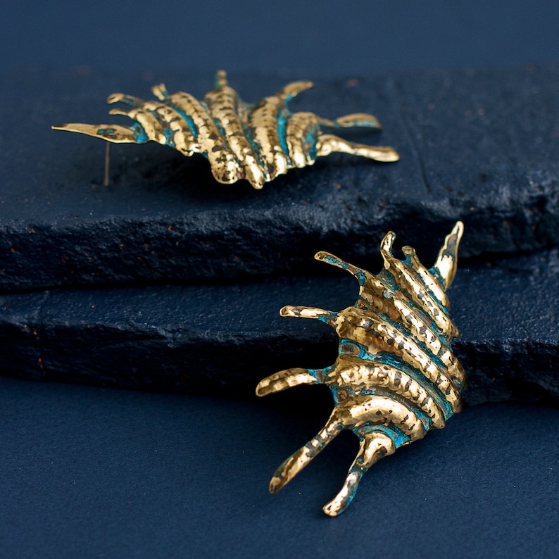 Bold earrings in the form of lond ribbed shell with spikes on the side. Earrings are hand-made from the brass sheet using hammers and other tools. These are stud earrings with silver ear wires.