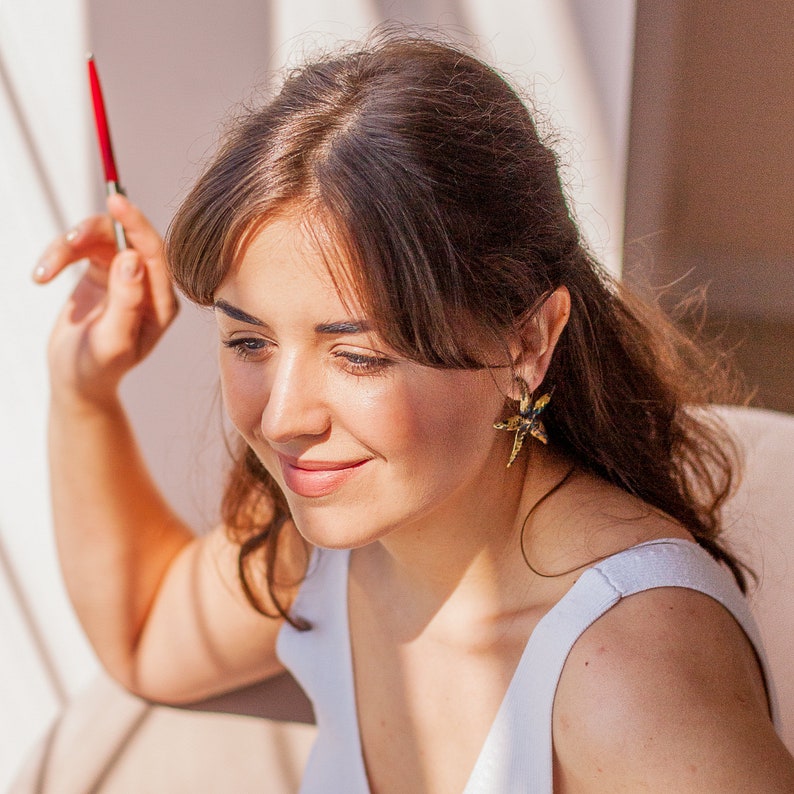 Woman in big golden brass starfish stud earrings. Earrings are not very big, but definitely noticable and eye-catching. These are stud earrings so they are fixed in the ear without dangling. Earrings are shiny and bold, they reflect the light.