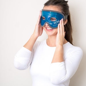 K&ouml;nnte beinhalten: Eine blaue Gel-Augenmaske mit einem grauen Band. Die Maske hat zwei Augenl&ouml;cher und den Text "H/M Hangover Mask" aufgedruckt.