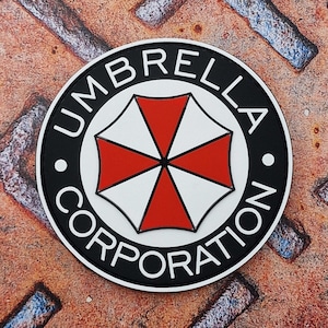 Könnte beinhalten: Ein schwarzer und weißer runder Patch mit dem Text "Umbrella Corporation" in einem weißen Kreis um ein rotes und weißes Regenschirmlogo.
