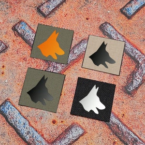 May include: Four different colored patches with a silhouette of a German Shepherd dog. The patches are orange, black, white, and tan.
