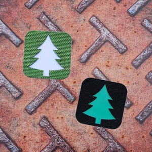 May include: Two square patches featuring a tree design. One has a white tree on a green background, the other a green tree on black. They are set against a rusty, patterned metal surface.