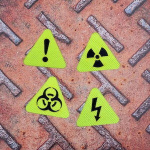 以下が含まれることがあります： 黒い記号が付いた4つのネオングリーンの三角形のパッチ。感嘆符、放射線記号、バイオハザード記号、稲妻。錆びた金属の表面に配置されています。