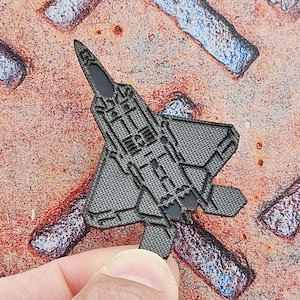 May include: A gray, detailed, cutout of an F-22 Raptor fighter jet. The jet is made of a textured material and has a realistic design.