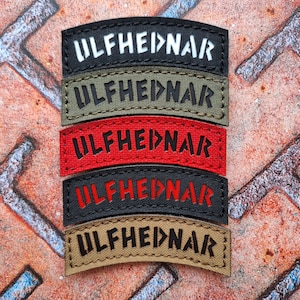 Può includere: Cinque toppe ricamate con il testo "ULFHEIDNAR" in diversi colori. Le toppe sono nere, verdi, rosse, nere e marroni.