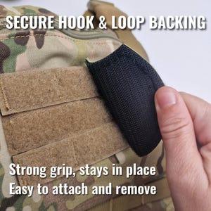 Op de afbeelding: Close-up van camouflage stof met klittenband. Een zwart klittenband patch wordt aan de stof bevestigd. Tekst luidt: "SECURE HOOK & LOOP BACKING", "Strong grip, stays in place" en "Easy to attach and remove."
