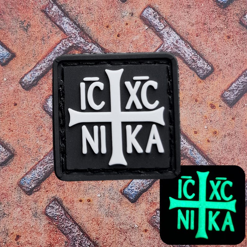 Pode incluir: Um patch quadrado preto com uma cruz branca e as palavras gregas "IC XC NIKA". Uma vers&atilde;o menor e verde brilhante do patch &eacute; mostrada abaixo. O patch est&aacute; em uma superf&iacute;cie met&aacute;lica enferrujada e texturizada.